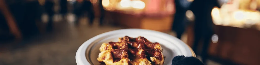 A warm, freshly made waffle drizzled with caramel sauce at the Galway Christmas Market, with festive lights and market stalls in the background. | The Dawson Hostel