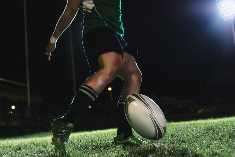 Connacht rugby player kicking a ball during a night match, with affordable accommodation for rugby fans at The Dawson Hostel Galway.