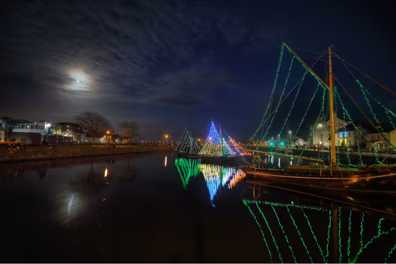 Traditional Galway Hooker boats lit up in green, white, and blue at The Claddagh for St. Patrick’s Day celebrations. Find affordable St. Patrick’s Day accommodation in Galway at The Dawson Hostel—central, social, and budget-friendly.